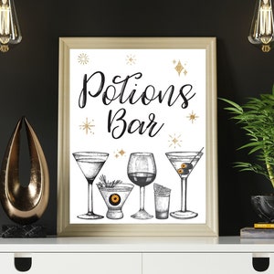 May include: A framed "Potions Bar" print with illustrations of cocktails. The print is displayed on a white table with decorative items, including a gold sculpture, a small elephant statue, and a potted plant. Overhead, there are hanging light fixtures.