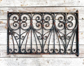 May include: A black wrought iron window grate with a decorative scroll design. The grate is slightly rusted and has a vintage look.