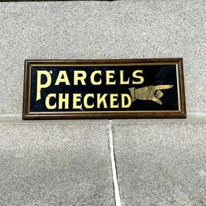 Puede incluir: Un letrero de madera vintage con fondo negro y letras doradas que dice "PARCELS CHECKED" con una mano dorada apuntando.