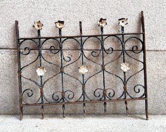 May include: A black metal fence with decorative scrolls and white flower accents. The fence is made of wrought iron and has a rustic look.