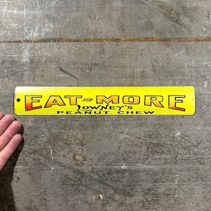 May include: Yellow metal ruler with the text "EAT-MORE LOWNEY'S PEANUT CHEW" printed on it.