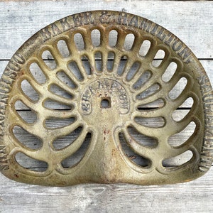 Könnte beinhalten: Ein antiker Traktorsitz aus Gusseisen mit einem dekorativen Design und dem Text "San Francisco Maker & Hamilton, San Francisco" am Rand.