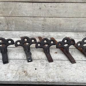 Puede incluir: Cinco soportes de metal negro antiguo con un diseño decorativo. Los soportes están en una fila sobre una superficie de madera.