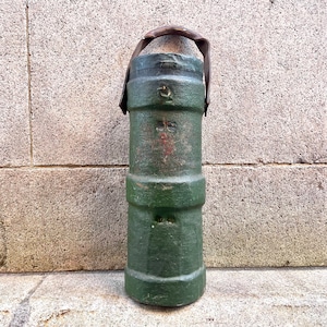 May include: A green metal cylinder with a leather handle. The cylinder has a worn, distressed look and is likely an antique.