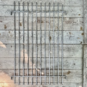 Puede incluir: Una valla de metal plateado con barras verticales, montada sobre una superficie de madera blanca.