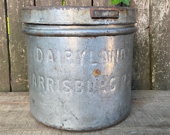 May include: A vintage metal container with a lid. The container is silver with a faded gray paint finish. The container has the words "Dairymaid Harrisburg" embossed on the side.