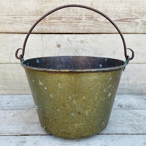 May include: A vintage brass bucket with a rusty metal handle. The bucket has a worn, green patina and is perfect for rustic decor.