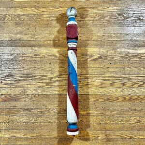May include: A vintage barber pole with red, white, and blue stripes. The pole is made of wood and has a rounded top.