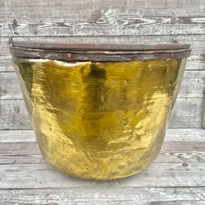 May include: A large, antique brass planter with a hammered finish. The planter has a rounded shape and a wide, flat rim.