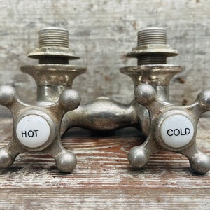 Könnte beinhalten: Antiker, silberfarbener Wasserhahn für heißes und kaltes Wasser mit Porzellanknöpfen, die mit "HOT" und "COLD" beschriftet sind.