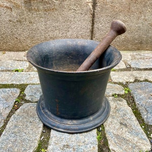 May include: A black cast iron mortar and pestle set. The mortar is round and has a wide base. The pestle is long and has a rounded end.