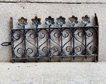 May include: A black metal fence with a decorative design featuring flower-shaped finials. The fence is rusty and has a distressed look.