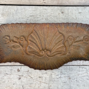 May include: A rustic, cast iron planter with a scalloped edge and a decorative design of two stylized seashells and floral motifs.