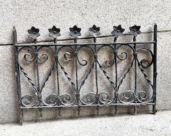 May include: Black wrought iron fence with decorative floral accents and a heart-shaped design. The fence is made of twisted metal and has a weathered finish.