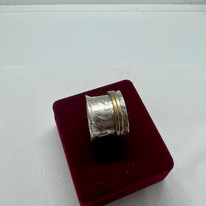 May include: A silver ring with a textured surface and a gold band. The ring is displayed on a red velvet box.
