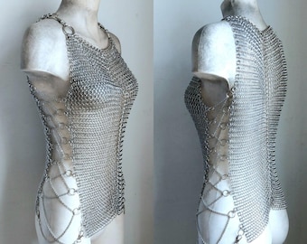 Könnte beinhalten: Ein silbernes Kettenhemd-Oberteil mit einem Halterneck und einem Kreuzdesign an den Seiten. Das Oberteil besteht aus kleinen, ineinandergreifenden Metallringen.