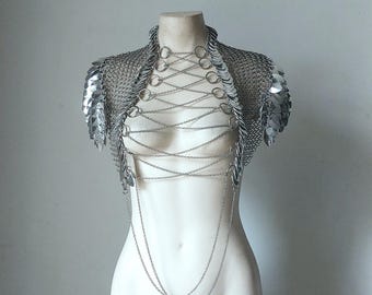 Könnte beinhalten: Silbernes Kettenhemd-Oberteil mit einer silbernen Kettenkette und dekorativen silbernen Kreisen. Das Oberteil hat ein kurzärmliges Design und ist aus Metall.