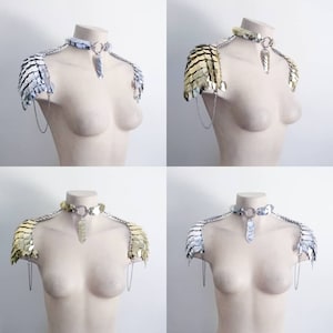 Op de afbeelding: Een zilveren en gouden kettingmail choker met bijpassende schouderstukken. De schouderstukken zijn gemaakt van kleine, overlappende metalen schubben. De choker heeft een hanger in de vorm van een traan.