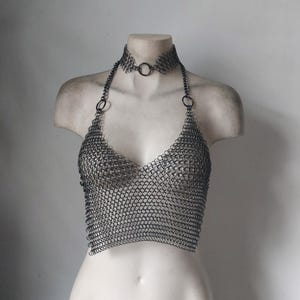 May include: A silver chainmail top with a matching choker necklace. The top is a halter style with a V-neckline and is made of small, interlocking metal rings.