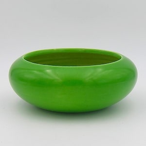 May include: A bright green ceramic bowl with a rounded shape. The bowl is smooth and glossy.