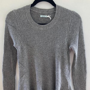 May include: Gray ribbed sweater with a ruffled hem and long sleeves. The sweater has a round neckline and a small white tag with the text "A New Day" on it.