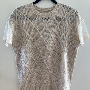 May include: A beige knitted sweater with a diamond pattern and lace sleeves.