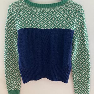 May include: A green and white patterned sweater with a navy blue bottom half. The sweater has long sleeves and a crew neck.