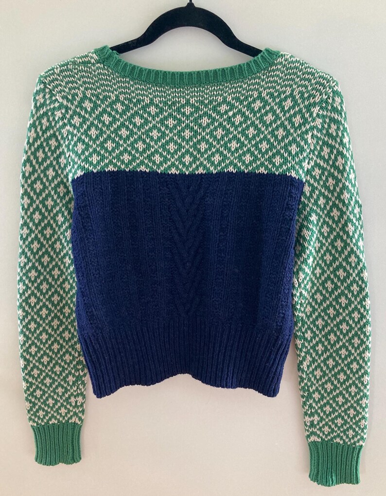 May include: A green and white patterned sweater with a navy blue bottom half. The sweater has long sleeves and a crew neck.