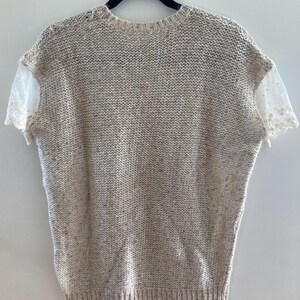 May include: A beige knitted sweater with short sleeves and a lace trim on the sleeves.