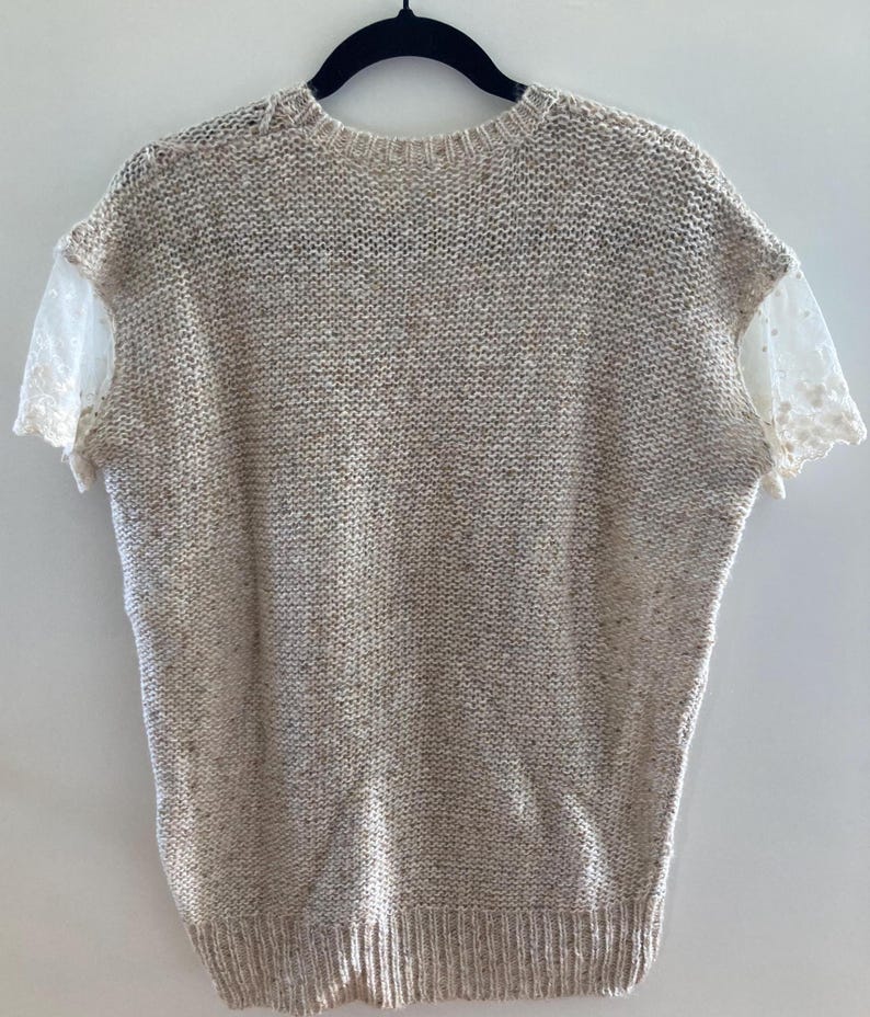 May include: A beige knitted sweater with short sleeves and a lace trim on the sleeves.