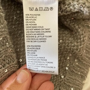 Op de afbeelding: Een wit waslabel met zwarte tekst met details over de stofsamenstelling en wasinstructies voor een kledingstuk. Het label vermeldt: 45% Polyester, 21% Acryl, 16% Nylon, 12% Wol, 6% Mohair. Handwas koud, niet wringen of draaien, alleen chloorvrij bleekmiddel gebruiken indien nodig, in vorm brengen en plat laten drogen, strijken op lage temperatuur indien nodig, chemisch reinigen mogelijk. 45% Polyester, 21% Acryl, 16% Nylon, 12% Wol, 6% Mohair. Handwas koud, niet wringen of draaien, alleen chloorvrij bleekmiddel gebruiken indien nodig, in vorm brengen en plat laten drogen, strijken op lage temperatuur indien nodig, chemisch reinigen mogelijk.