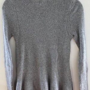 May include: A gray ribbed knit sweater with a ruffled hem.