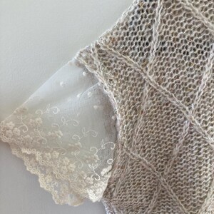 May include: A beige knitted sweater with a lace trim on the sleeves. The sweater has a cable knit pattern.