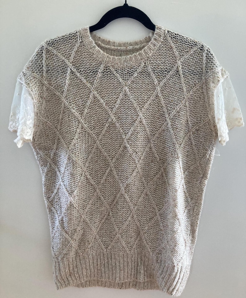 May include: A beige knitted sweater with a diamond pattern and lace sleeves.