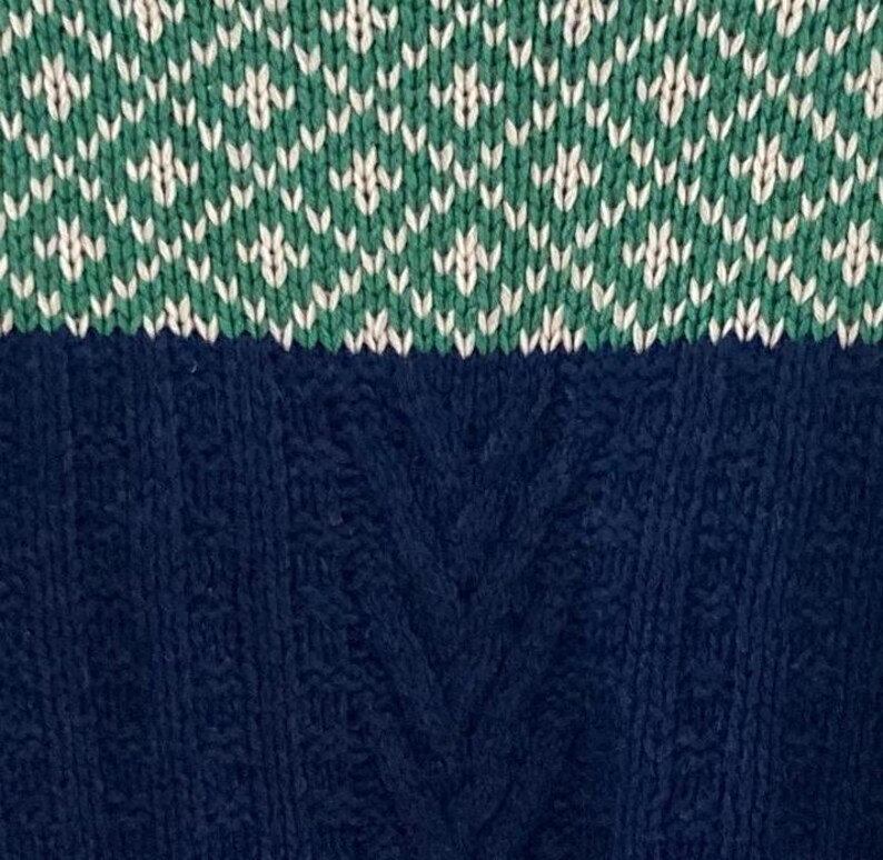 May include: A blue and green knitted sweater with a cable knit pattern on the bottom half and a diamond pattern on the top half.