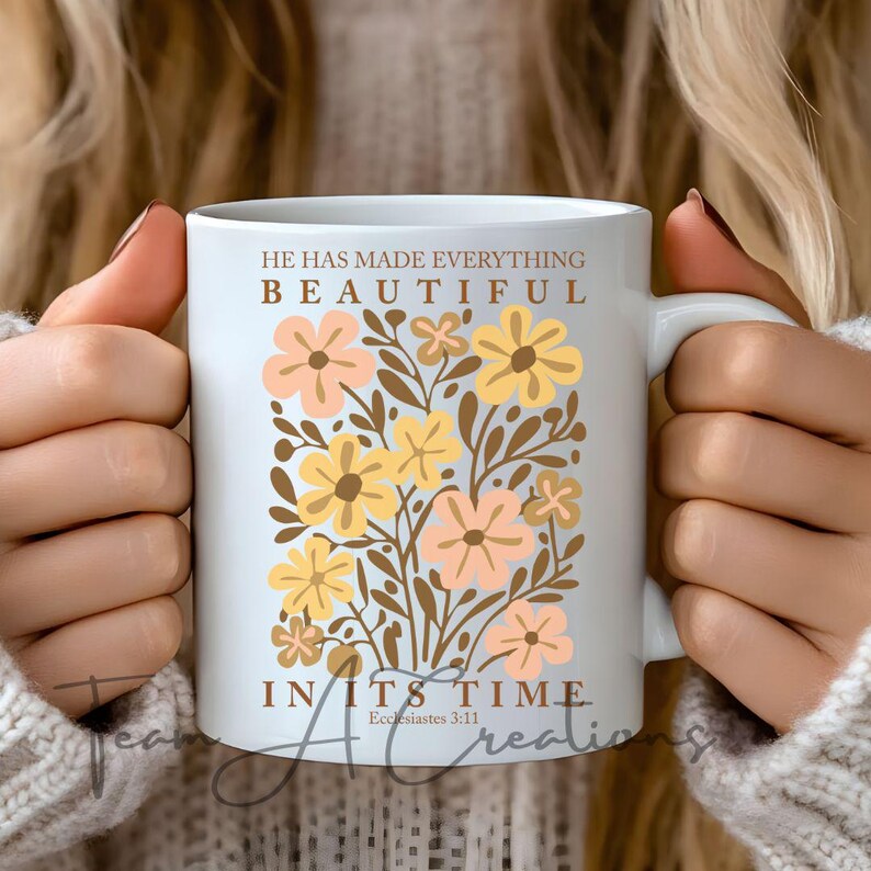 Puede incluir: Taza de cer&aacute;mica blanca con un dise&ntilde;o floral en tonos amarillos y rosas. El texto "&Eacute;l ha hecho todo hermoso en su tiempo" est&aacute; impreso en la taza, con la referencia b&iacute;blica "Eclesiast&eacute;s 3:11" debajo.