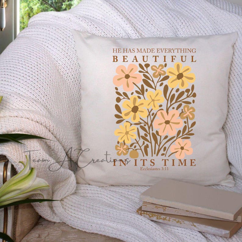 Puede incluir: Una almohada blanca con un dise&ntilde;o floral en tonos amarillos y melocot&oacute;n. La almohada presenta el texto "&Eacute;l ha hecho todas las cosas hermosas en su tiempo, Eclesiast&eacute;s 3:11".