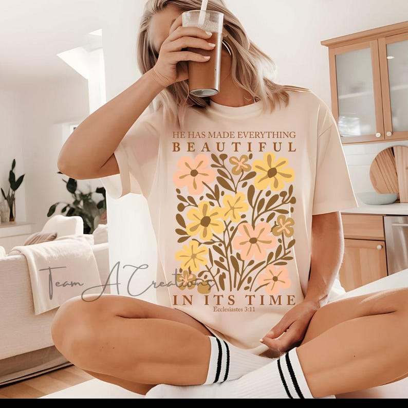 Puede incluir: Una camiseta beige con un dise&ntilde;o floral y el texto "&Eacute;l ha hecho todo hermoso en su tiempo, Eclesiast&eacute;s 3:11".