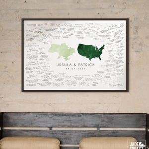 May include: A framed wedding guest book alternative featuring green and light green map outlines of the United States and Ukraine. The names "URSULA & PATRICK" and the date "09.07.2024" are printed below the maps. The white background is filled with handwritten signatures.