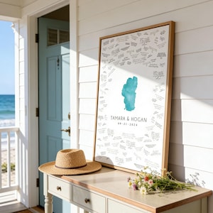 May include: A rectangular framed guest book print featuring a central teal watercolor map of Lake Tahoe, surrounded by handwritten signatures. The text reads TAMARA & HOGAN and 09-21-2024 in black ink on a white background, encased in a light wood frame.