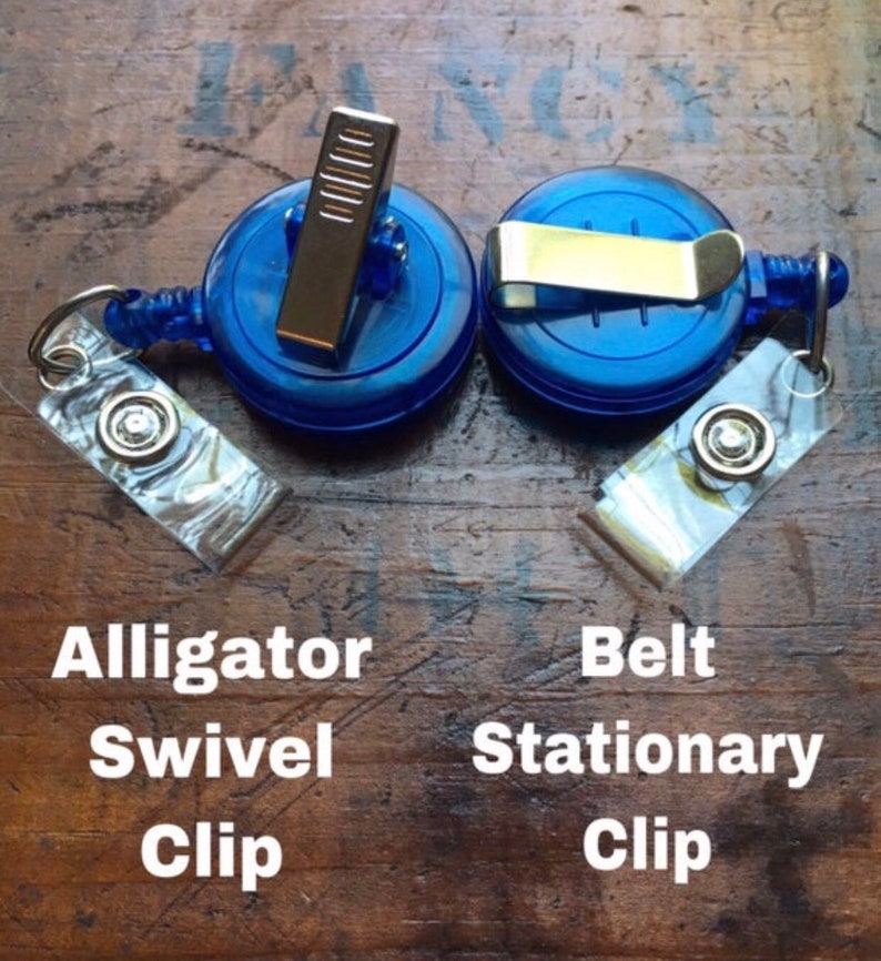 May include: Two blue retractable badge reels with different clip styles: an alligator swivel clip and a belt stationary clip. Each reel has a clear, decorative tag attached. The text on the image reads "Alligator Swivel Clip" and "Belt Stationary Clip."