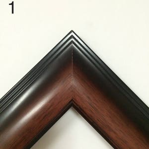 May include: Close-up of a corner of a picture frame. The frame has a dark brown wood grain interior and a black exterior. The number "1" is in the upper left corner of the image.