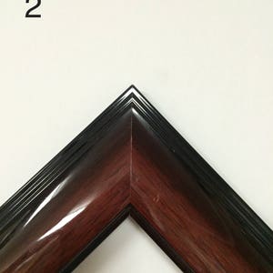 May include: A corner of a picture frame with a glossy, dark wood grain finish. The frame has a black outer edge and a number "2" in the upper left corner. The frame is angled, showcasing its polished surface.