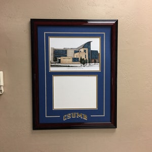 May include: A framed print of a building with a blue background and a gold inscription that reads "CSUMB".