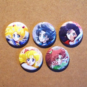 May include: Five round, colourful buttons featuring anime characters from the Sailor Moon series. Each button has a different character with a unique pose and expression. The buttons are perfect for fans of the show.