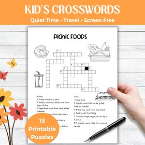 May include: Black and white printable crossword puzzle titled "Picnic Foods" with a donut, drink, and sandwich illustrations. The text "Kid's Crosswords" is at the top. A hand holds the puzzle with a pen.