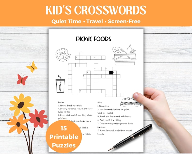 May include: Black and white printable crossword puzzle titled "Picnic Foods" with a donut, drink, and sandwich illustrations. The text "Kid's Crosswords" is at the top. A hand holds the puzzle with a pen.