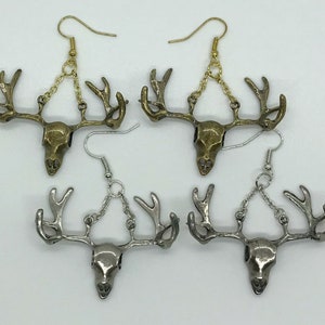 May include: Four pairs of antler skull earrings. Two pairs are bronze-toned with gold-colored ear wires and chains. The other two pairs are silver-toned with silver-colored ear wires and chains. The earrings are displayed on a white background.