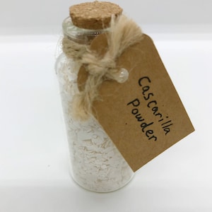 May include: A small glass bottle with a cork stopper filled with white powder. A brown paper tag is tied around the bottle with twine and reads "Cascarilla Powder".