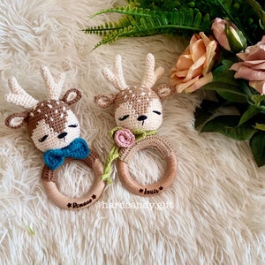 May include: Two crocheted deer rattle toys with wooden rings. The rings are engraved with the names "Roman" and "Louis".